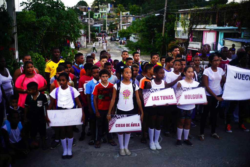 Niños locales sostienen carteles con los nombres de las provincias de las que proceden los jóvenes luchadores (detrás de ellos) que participan en el torneo de lucha. Foto: Ramón Espinosa / AP.