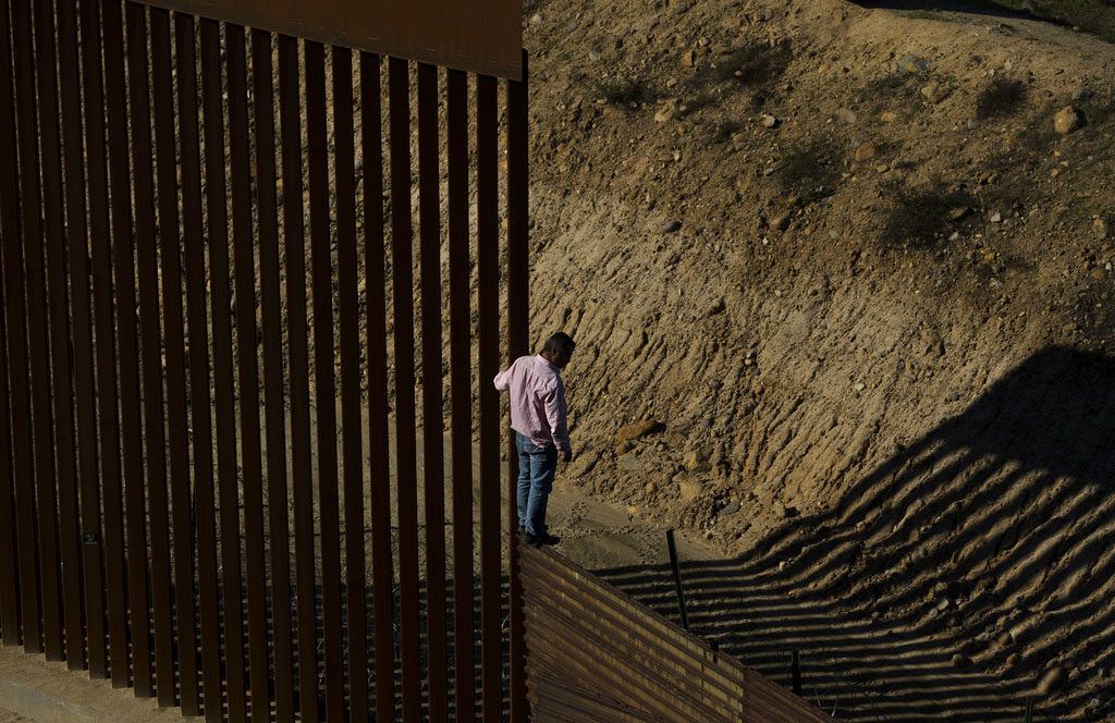 Un migrante se para en la valla fronteriza antes de saltar al lado de Estados Unidos, hacia San Diego, California, desde Tijuana, México, el viernes 28 de diciembre de 2018. Foto: Daniel Ochoa de Olza / AP.