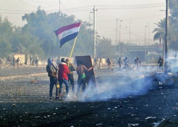 Protesters waving the national flag while security forces launch tear gas at a protest in central Baghdad, Iraq, on Monday, January 20, 2020. Photo: AP/Hadi Mizban