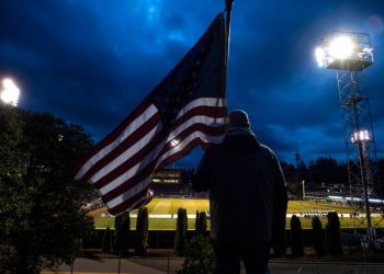 A man holds the United States flag while following a United States Football League game in Tacoma, Washington. Photo: Joshua Bessex/The News Tribune via AP.