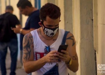 A Cuban checks his cell phone using a facemask in Havana, as a protection measure against the COVID-19 pandemic. Photo: Otmaro Rodríguez.