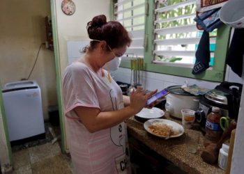 A woman checks her phone in the kitchen of her home on April 6, 2020 in Havana. Photo: EFE/Ernesto Mastrascusa