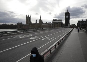 A person with a face mask walks across the nearly empty Westminster Bridge with Parliament in the background. London, Friday March 20, 2020. Photo: Matt Dunham/AP.