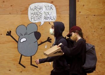 A man and a woman wearing facemasks walk past a mural reminding people to wash their hands, on a plank-protected store in San Francisco. Photo: Jeff Chiu/AP