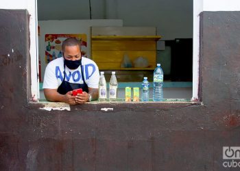 A clerk wearing a mask checks his mobile phone, after the relaxation of restrictions due to COVID-19 in Havana. Photo: Otmaro Rodríguez.