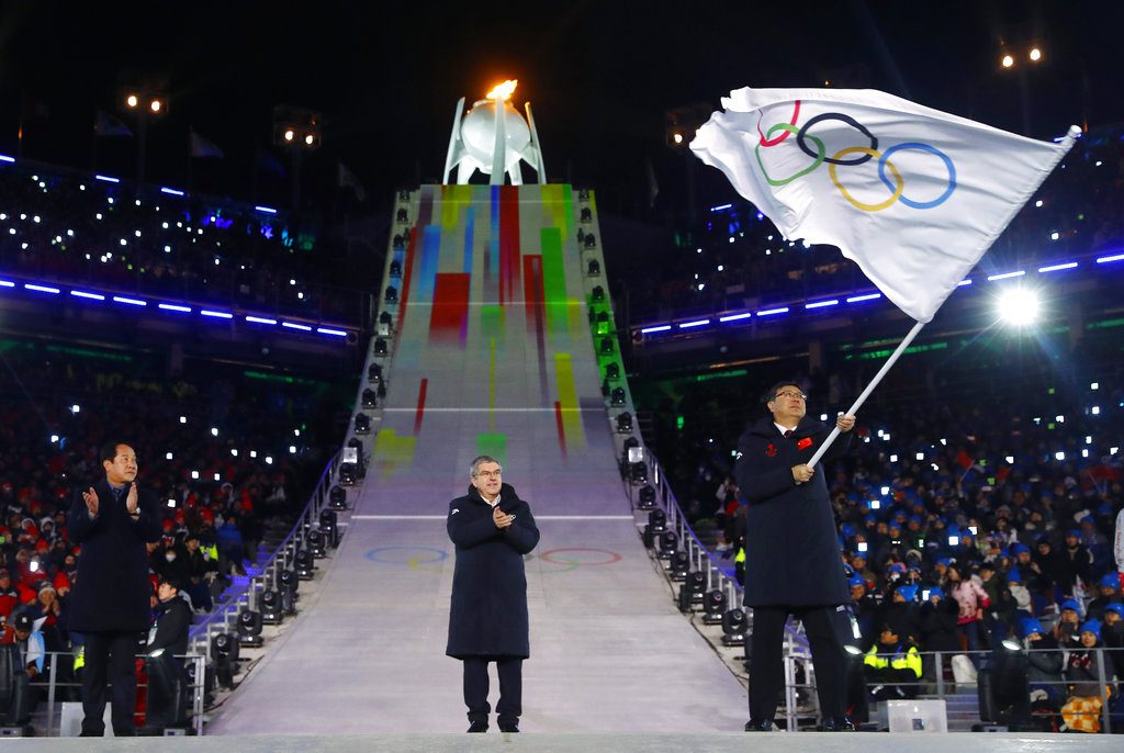 Thomas Bach (centro), presidente del Comité Olímpico Internacional, aplaude mientras Chen Jining, alcalde de Beijing, agita la bandera olímpica en la ceremonia de clausura de los Juegos de Invierno en Pyeongchang. Foto: Kai Pfaffenbach/Pool Photo via AP.