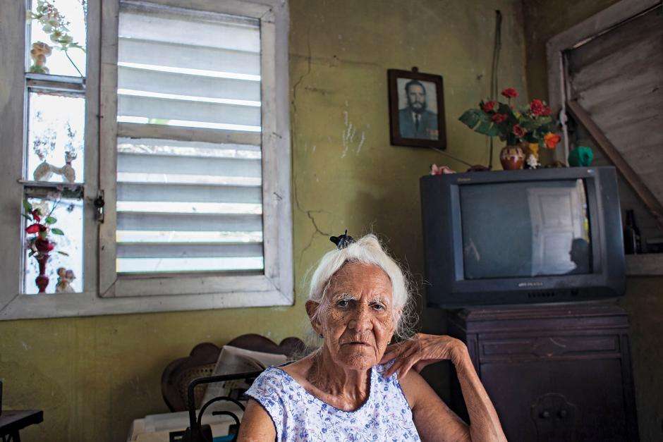 Justina Cordero Mesa, 90, in her home in Parraga, Havana, February 21, 2014, before her television was stolen. Mesa says of the Fidel photo on her wall that her late husband was a police officer, working for the government, he revered Fidel and placed his photo on the wall years ago. Now she says, “it just stayed there.” / Photo: Lisette Poole for Newsweek