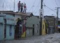Tres jóvenes observan desde un techo una calle inundada hoy, jueves 7 de septiembre, en Santiago de los Caballeros (República Dominicana). Foto: EFE / Luis Tavarez.