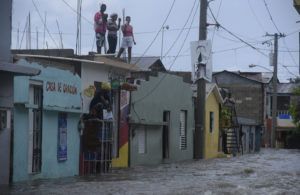 Tres jóvenes observan desde un techo una calle inundada hoy, jueves 7 de septiembre, en Santiago de los Caballeros (República Dominicana). Foto: EFE / Luis Tavarez.