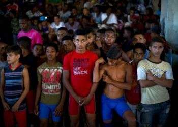 Jóvenes luchadores escuchan la oración de un sacerdote en la ceremonia de apertura de una competición de lucha de nivel aficionado en Chicharrones, Santiago de Cuba. Foto: Ramón Espinosa / AP.