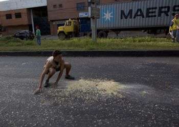 Un joven recoge granos de maíz que cayeron de un camión fuera del puerto de Puerto Cabello, Venezuela. Foto: Fernando Llano / AP.