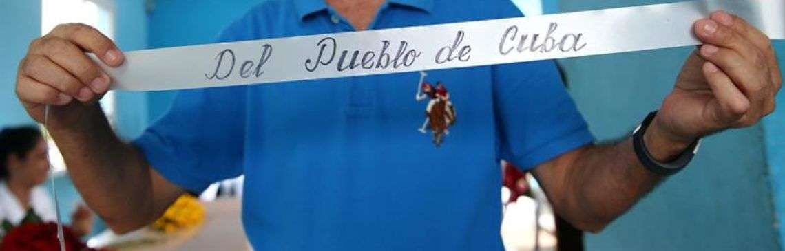 El profesor Carlos Parra rotula cuidadosamente dedicatorias en las coronas que acompañan las urnas de los fallecidos en el desastre aéreo que el viernes pasado enlutó la provincia cubana de Holguín, que perdió 67 hijos en el siniestro. Foto: Alejandro Ernesto/EFE.