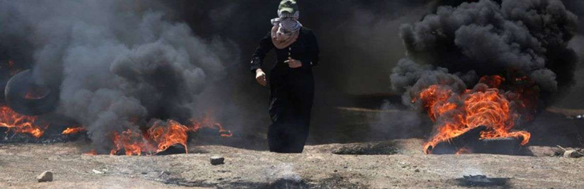 Una mujer palestina atraviesa una densa nube de humo negro provocada por la quema de neumáticos durante las protestas en la frontera entre la Franja de Gaza e Israel. Foto: Khalil Hamra / AP.
