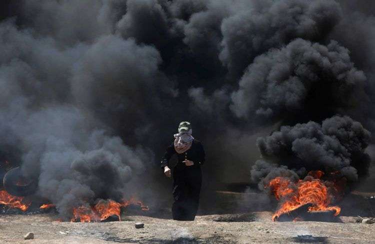 Una mujer palestina atraviesa una densa nube de humo negro provocada por la quema de neumáticos durante las protestas en la frontera entre la Franja de Gaza e Israel. Foto: Khalil Hamra / AP.