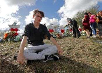 Chris Grady, estudiante de la escuela secundaria Marjory Stoneman Douglas, posa en un memorial en el exterior del centro donde el 14 de febrero de 2018 un pistolero provocó una balacera que causó 17 muertos, en Parkland, Florida. Foto: Gerald Herbert / AP.