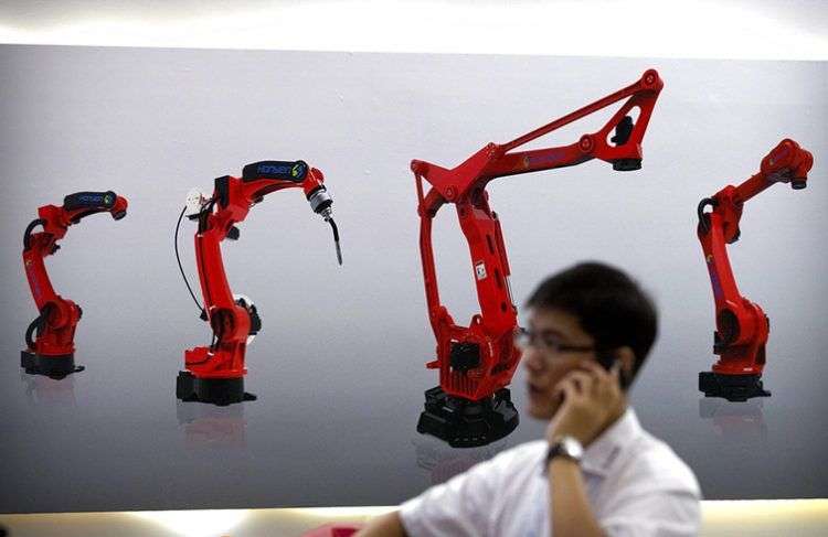 Un visitante habla por su smartphone delante de una imagen de robots de la empresa china Honyen, en el World Robot Conference, en Beijing, China. Foto: Mark Schiefelbein / AP.