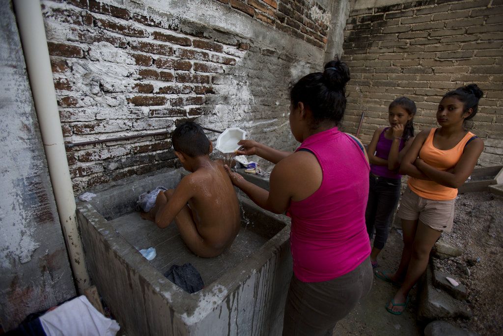 Una guatemalteca ducha a su hijo en un fregadero al exterior, en la propiedad de una iglesia que ofrece seguridad, comida donada, juguetes y ropa a las mujeres migrantes con hijos en Arriaga, México, el 26 de octubre de 2018. (AP Foto/Rebecca Blackwell)