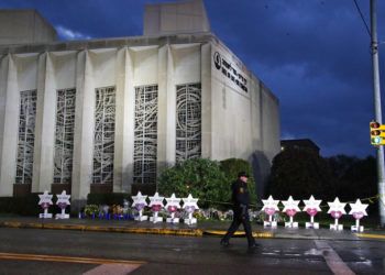 Un policía de Pittsburgh camina junto a la sinagoga Árbol de la Vida y una serie de flores y estrellas colocados en memoria de las víctimas de un hombre que se puso a disparar en el interior, el domingo 28 de octubre de 2018. Foto: Gene J. Puskar / AP.