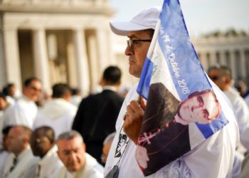 Un hombre sostiene un banderín con la imagen del arzobispo salvadoreño Oscar Romero antes de la ceremonia de canonización en su honor, en la Plaza de San Pedro en el Vaticano, este domingo 14 de octubre del 2018. Foto: Andrew Medichini / AP.