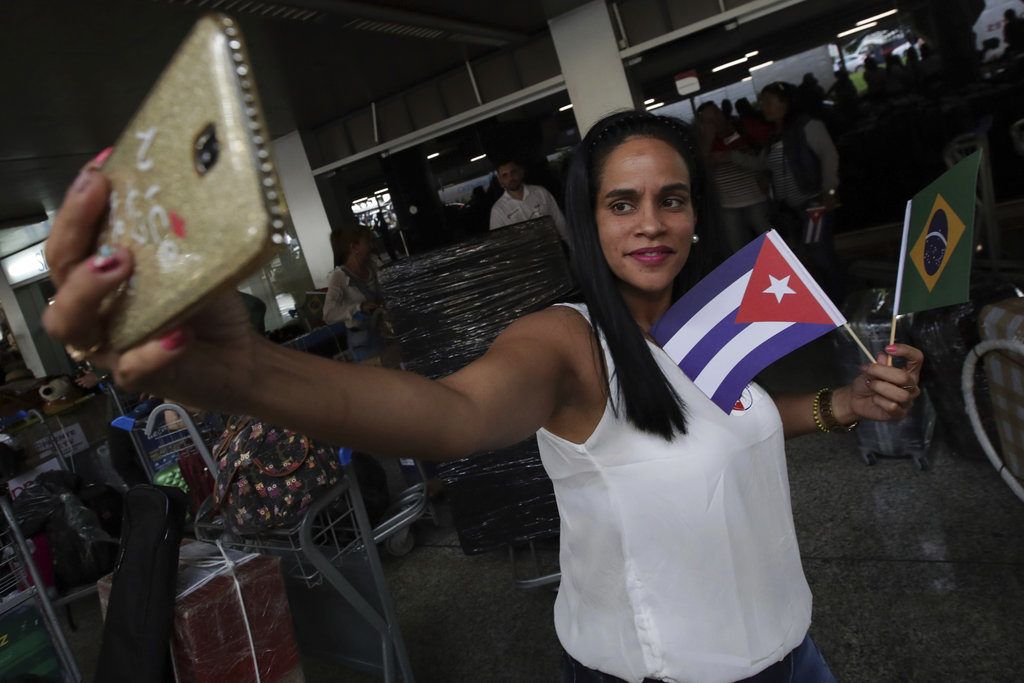 Una doctora cubana sosteniendo banderas de Cuba y Brasil se toma una selfie antes de que ella y otros médicos de su país regresen a casa desde el aeropuerto de Brasilia, Brasil, el jueves 22 de noviembre de 2018. (AP Foto/Eraldo Peres)