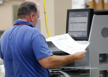 Un empleado de la oficina del Supervisor de Elecciones del condado de Broward pasa boletas por una máquina mientras cuenta votos de la elección legislativa del jueves 8 de noviembre de 2018 en Lauderhill, Florida. (AP Foto/Wilfredo Lee)