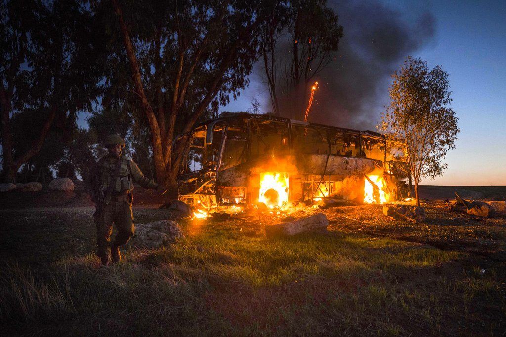 Un soldados israelí, junto a un autobús en llamas tras ser alcanzado por una bomba de mortero lanzada desde Gaza, cerca de la frontera con Israel, el 12 de noviembre de 2018. (AP Foto/Tsafrir Abayov)