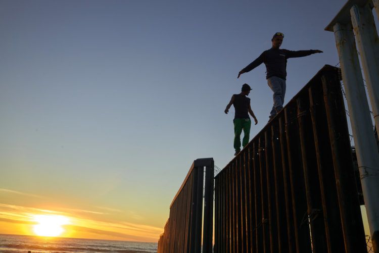 En esta imagen, tomada el 14 de noviembre de 2018, dos migrantes centroamericanos caminan sobre el muro que separa México de Estados Unidos, en Tijuana, México. Integrantes de una caravana de migrantes centroamericanos lograron llegar a la frontera estadounidense tras recorrer los últimos kilómetros de su largo viaje en buses y camiones. (AP Foto/Gregory Bull)