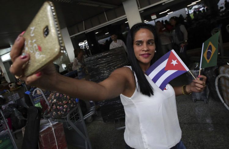 Una doctora cubana sosteniendo banderas de Cuba y Brasil se toma una selfie antes de que ella y otros médicos de su país regresen a casa desde el aeropuerto de Brasilia, Brasil, el jueves 22 de noviembre de 2018. Foto: Eraldo Peres / AP.