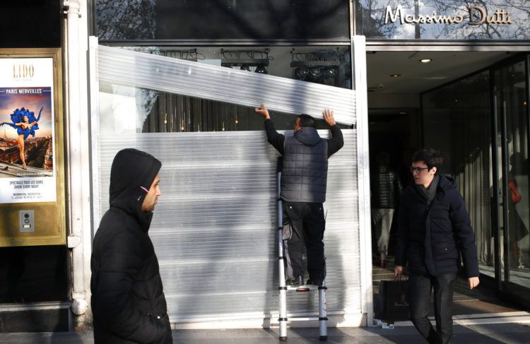 Un hombre protege el escaparate de una tienda en los Campos Elíseos, en París, el 14 de diciembre de 2018. Foto: Francois Mori / AP.