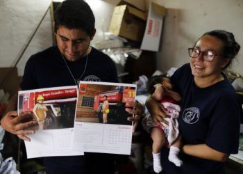 La bombera Fátima Olmedo (derecha) sostiene a su hija de dos meses Samara mientras su esposo, Rodrigo Giménez, muestra las páginas del calendario donde salen desnudos, en Asunción, Paraguay. Foto: Jorge Saenz / AP.