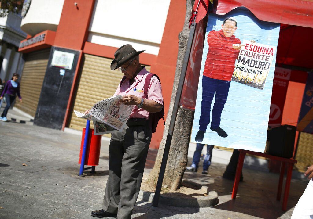 Un partidario del gobierno venezolano lee el periódico junto a un cartel con la imagen del exfallecido presidente Hugo Chávez con el lema "Esquina caliente, Maduro presidente", en Caracas, Venezuela, el 29 de enero de 2019. (AP Foto/Rodrigo Abd)