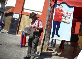 Un partidario del gobierno venezolano lee el periódico junto a un cartel con la imagen del exfallecido presidente Hugo Chávez con el lema "Esquina caliente, Maduro presidente", en Caracas, Venezuela, el 29 de enero de 2019. (AP Foto/Rodrigo Abd)