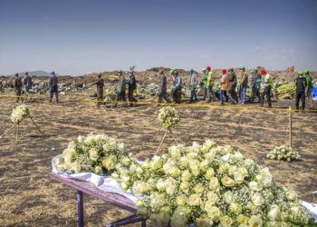 Un grupo de operarios pasa junto a las flores depositadas en el lugar donde se estrelló un Boeing 737 Max 8 de Ethiopian Airlines poco después de despegar con 157 personas a bordo, cerca de Bishoftu, o Debre Zeit, al sur de Adís Abeba, en Etiopía, el 13 de marzo de 2019. Foto: Mulugeta Ayene / AP.