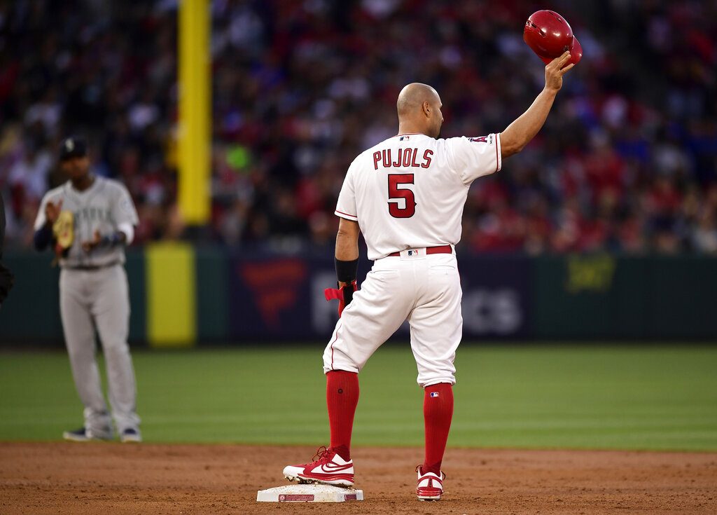 El dominicano Albert Pujols, de los Angelinos de Los Ángeles se quita el casco en un gesto a los fanáticos tras pegar un doble remolcador, mientras el campocorto de los Marineros de Seattle Tim Beckham aplaude al fondo, en el tercer inning de su juego de béisbol el sábado 20 de abril de 2019 en Anaheim, California. Con esa impulsada, Pujols empató con Babe Ruth en el 5to puesto de las tablas históricas de remolcadas con 1.992. Más tarde adelantó a Ruth con otra impulsada en el noveno. (AP Foto/Mark J. Terrill)