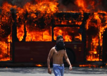 Un manifestante antigubernamental camina cerca de un autobús que fue incendiado por opositores al presidente de Venezuela, Nicolás Maduro, en Caracas, el martes 30 de abril de 2019.  Foto:  Fernando Llano / AP.