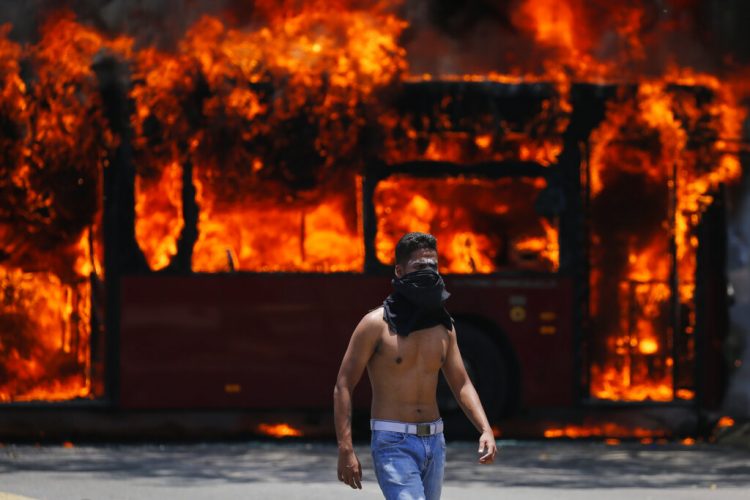Un manifestante antigubernamental camina cerca de un autobús que fue incendiado por opositores al presidente de Venezuela, Nicolás Maduro, en Caracas, el martes 30 de abril de 2019.  Foto:  Fernando Llano / AP.