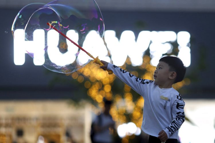 Un niño juega con pompas de jabón cerca del logo del gigante tecnológico chino Huawei, en Beijing, mayo de 2019. Foto: Ng Han Guan / AP.