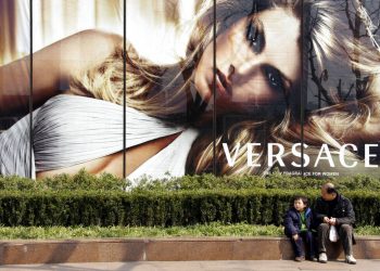 Fotografía de archivo del 15 de febrero de 2008 de un niño y un hombre sentados frente a una publicidad de Versace en Shanghái, China. (AP Foto/Eugene Hoshiko, Archivo)