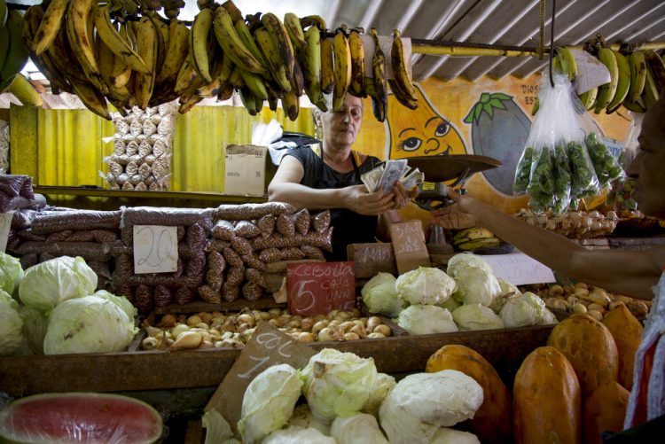 Una vendedora cuenta dinero luego de vender unas verduras a un cliente en su puesto en La Habana. Foto: Ismael Francisco / AP / Archivo.