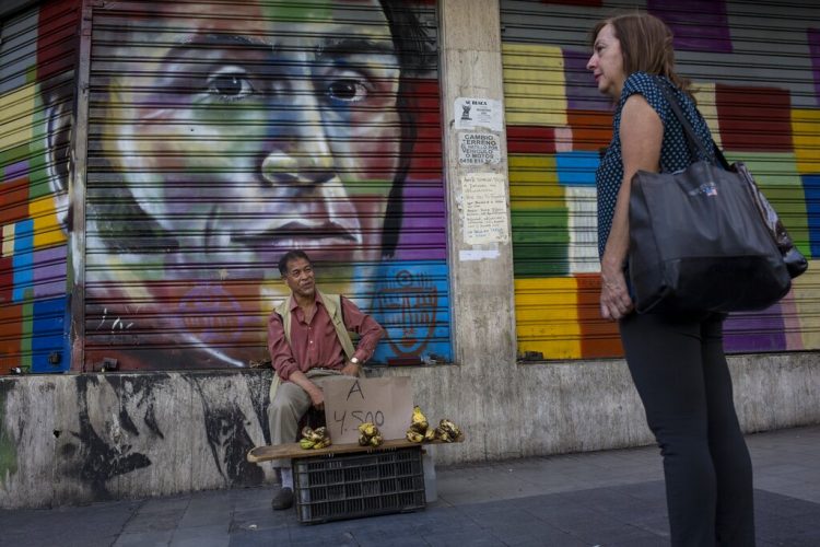 Un vendedor callejero ofrece bananas frente a una pintura de Simón Bolívar en Caracas, Venezuela. Foto: Rodrigo Abd/AP.