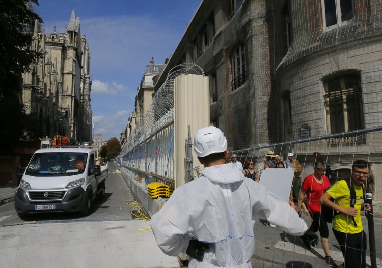 Un trabajador vestido con un overol blanco abre la puerta de la cerca que rodea a la catedral de Notre Dame, en París, el jueves 1 de agosto de 2019, mientras comienzan las labores preliminares para reparar los daños del incendio. Foto: Michel Euler / AP.