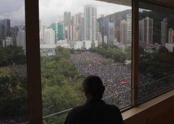 Una persona mira por una ventana a miles de manifestantes en el Parque Victoria en Hong Kong el domingo 18 de agosto del 2019. Foto: Kin Cheung / AP.