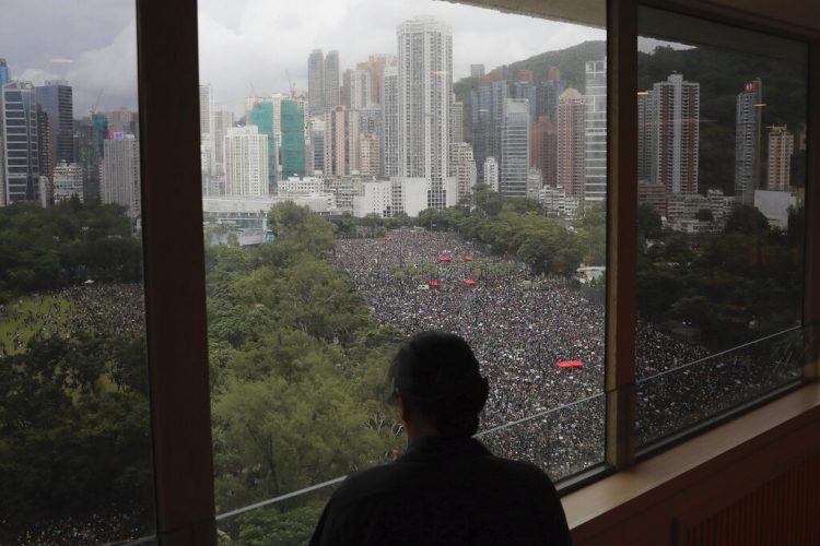 Una persona mira por una ventana a miles de manifestantes en el Parque Victoria en Hong Kong el domingo 18 de agosto del 2019. Foto: Kin Cheung / AP.