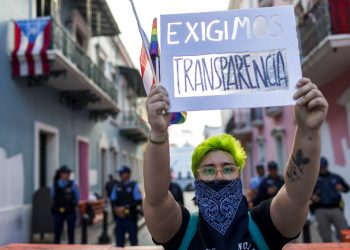 Un joven sostiene en lo alto un cartel durante una pequeña manifestación frente a La Fortaleza, la mansión del gobierno, en San Juan, Puerto Rico, el viernes 9 de agosto de 2019. (AP Foto/Dennis M. Rivera Pichardo)