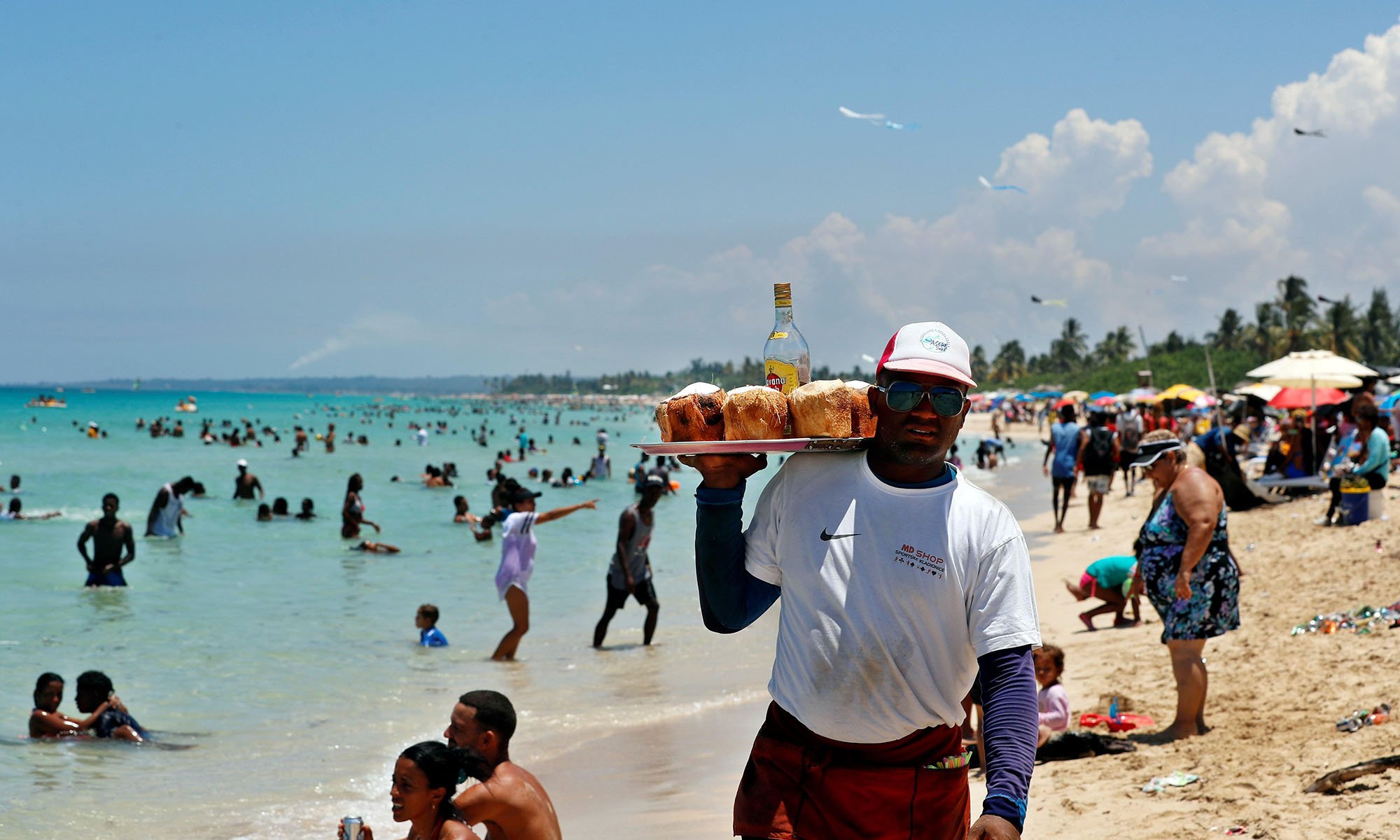 Un hombre vende agua de coco con ron a los bañistas en una playa del litoral norte de La Habana este verano. Foto: Ernesto Mastrascusa / EFE.