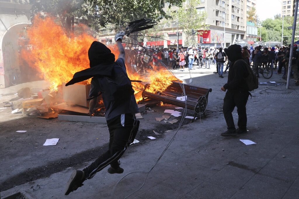 Un manifestante antigubernamental arroja un retrato del presidente Sebastián Piñera a una barricada en llamas en Santiago de Chile, durante las protestas de las últimas semanas en ese país sudamericano. Foto: Rodrigo Abd / AP / Archivo.