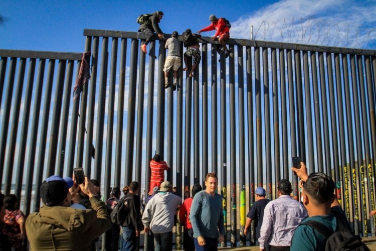 Un grupo de inmigrantes intenta saltar el muro metálico en la frontera con San Diego. Foto: Joebeth Terrique / EFE / Archivo.
