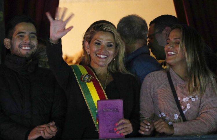 La segunda vicepresidenta del Senado de Bolivia y senadora de la oposición Jeanine Áñez, en el centro, saluda a la multitud ataviada con la banda presidencial en el balcón del palacio de Quemado, tras proclamarse presidenta interina del país, en la Paz, Bolivia, el martes 12 de noviembre de 2019. Foto: Juan Karita / AP.