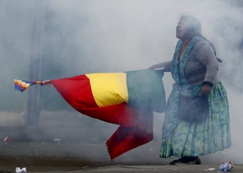 En esta imagen, tomada el 13 de noviembre de 2019, una seguidora del expresidente de Bolivia Evo Morales porta una bandera nacional durante disturbios con la policía, en La Paz, Bolivia. (AP Foto/Natacha Pisarenko)