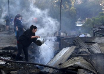 Residentes arrojan agua sobre los restos de sus casas el miércoles 25 de diciembre de 2019, después que un incendio dañó decenas de viviendas en las afueras de Valparaíso, Chile. Foto: Raul Zamora/Aton Chile vía AP.